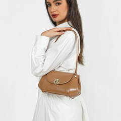 شنطة نسائية من ساغا باللون البني الكراميل تُرتدى على الكتف بأسلوب راقٍ، تضيف لمسة أنثوية مميزة على الفستان الأبيض.