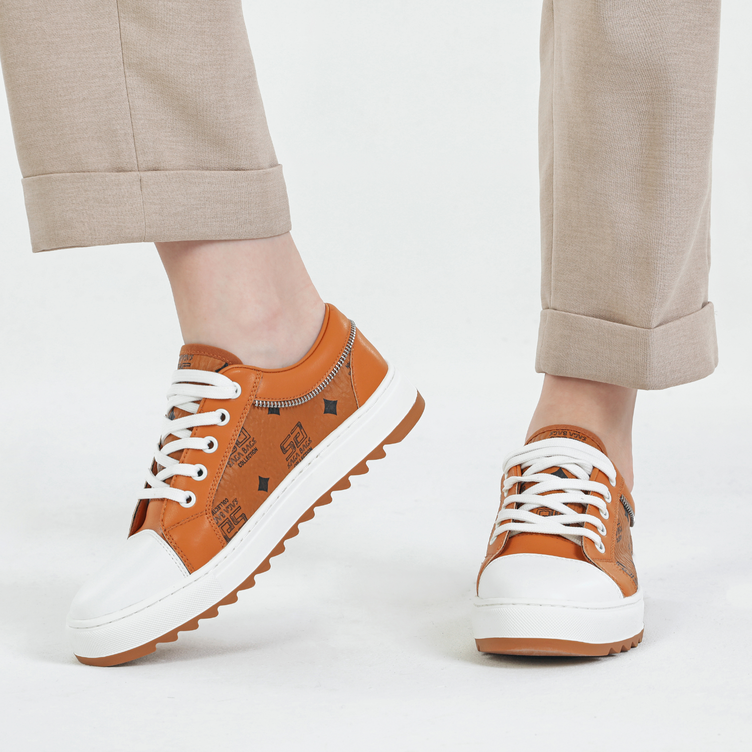 عرض جانبي لحذاء رياضي نسائي من الجلد البرتقالي مع نعل أبيض وتفاصيل سوداء من مجموعة ساغا